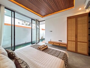 A modern hotel room with a large bed, a sliding glass door to a balcony, and a traditional wooden wardrobe. - Sudut Padi Villas Ubud (Ubud)