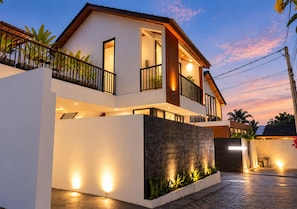 A modern two-story house with a balcony, a well-lit entrance, and a paved driveway. - Sudut Padi Villas Ubud (Ubud)