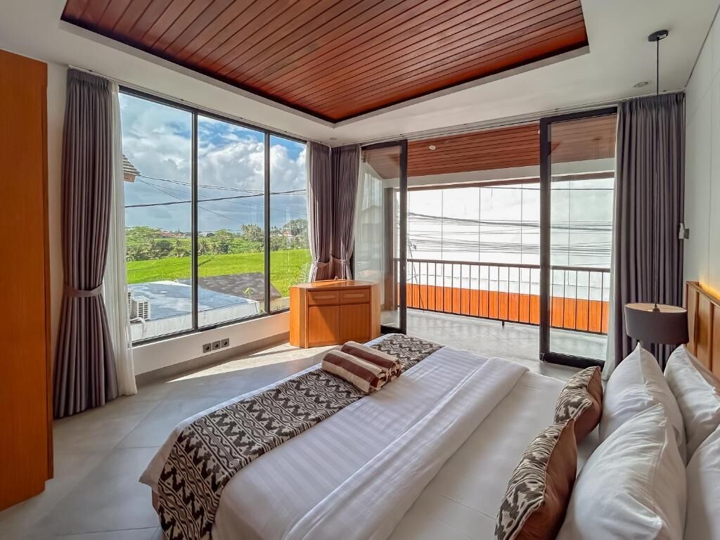 Une chambre moderne avec un grand lit, un plafond en bois et un balcon offrant une vue sur la verdure.