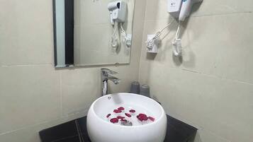 A bathroom with a round white sink, a mirror, a hairdryer, and a towel rack.