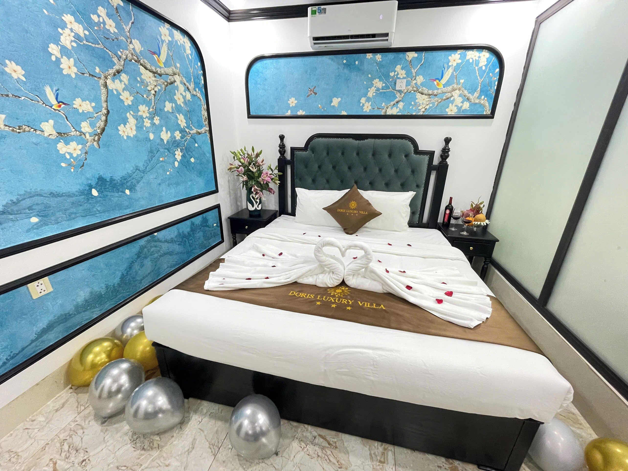 A bedroom with a bed, a nightstand, a vase of flowers, and a wall with a blue floral design.