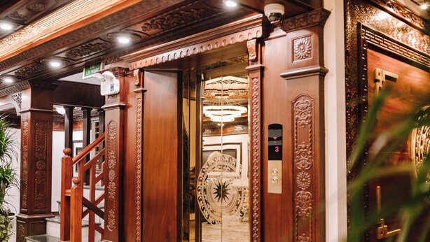 Um elevador ornamentado com design clássico, piso de mármore e escadaria que leva a uma entrada.