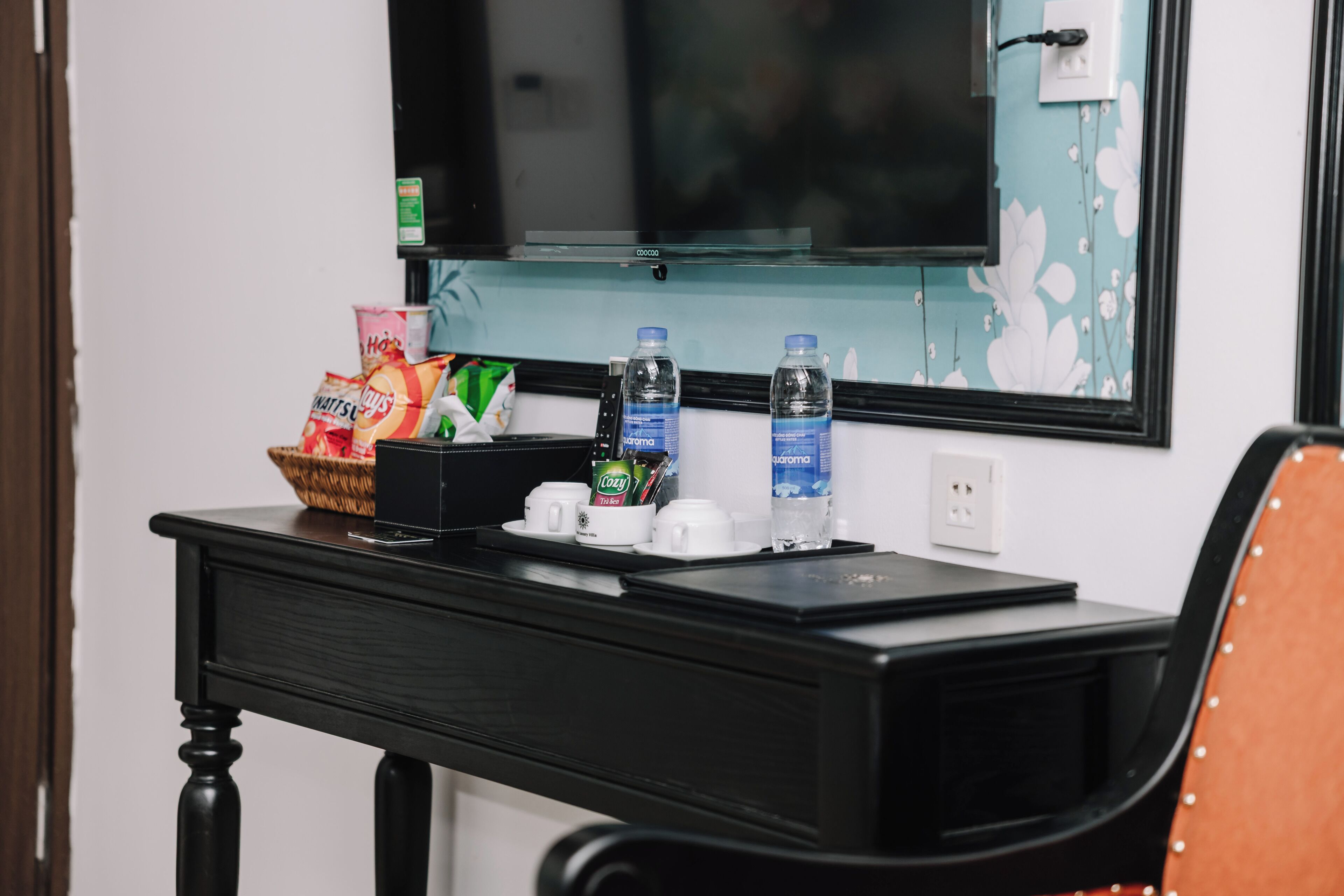 Ett hotellrum med ett svart skrivbord, en tv och en korg med snacks.