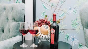 A table with two wine glasses, a bottle of wine, a decorative fruit bowl, and a plush armchair.