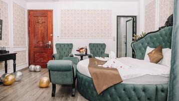 A hotel room with a green upholstered bed, a red door, a small table with a vase, and a green armchair.