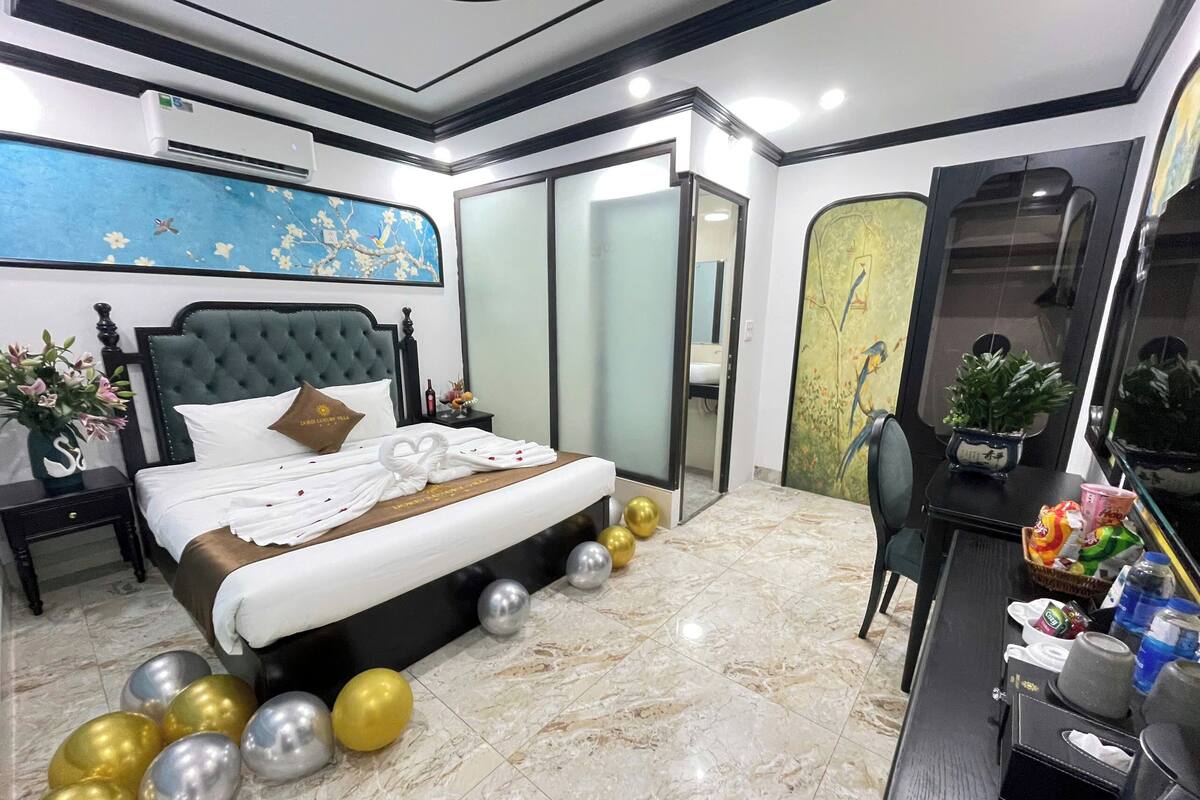 Ein Hotelzimmer mit Bett, Schreibtisch, Stuhl, einer Blumenvase und einem Bild an der Wand.