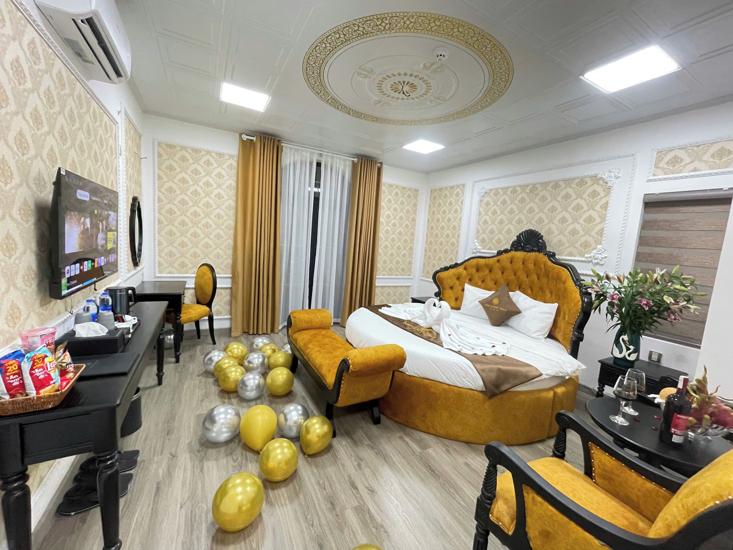 A hotel room with a bed, a desk, a television, a dining table, and a vase with flowers.