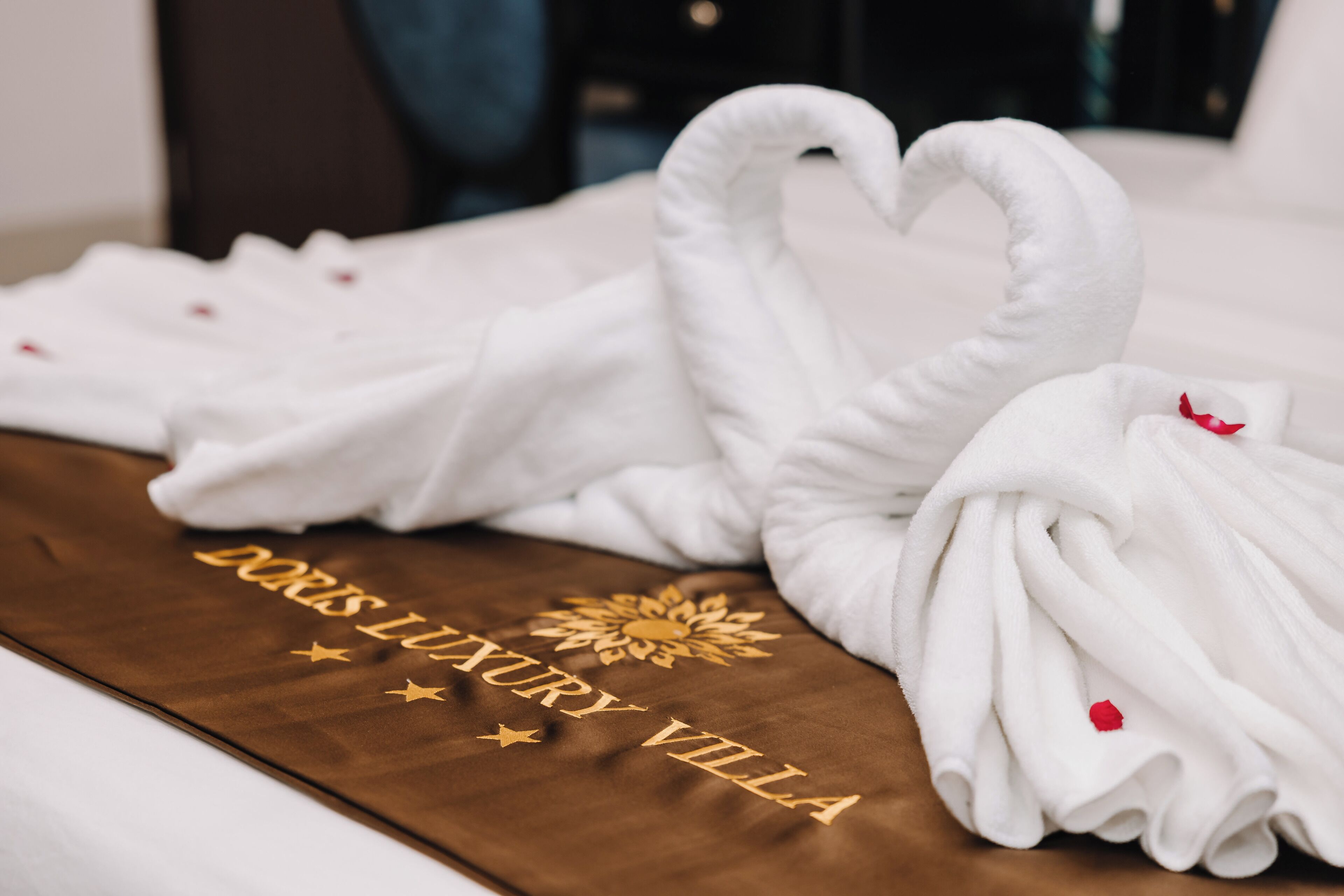 A bed with white towels arranged in swan shapes, a brown headboard, and a decorative emblem with the text 'Luxury Villa.'