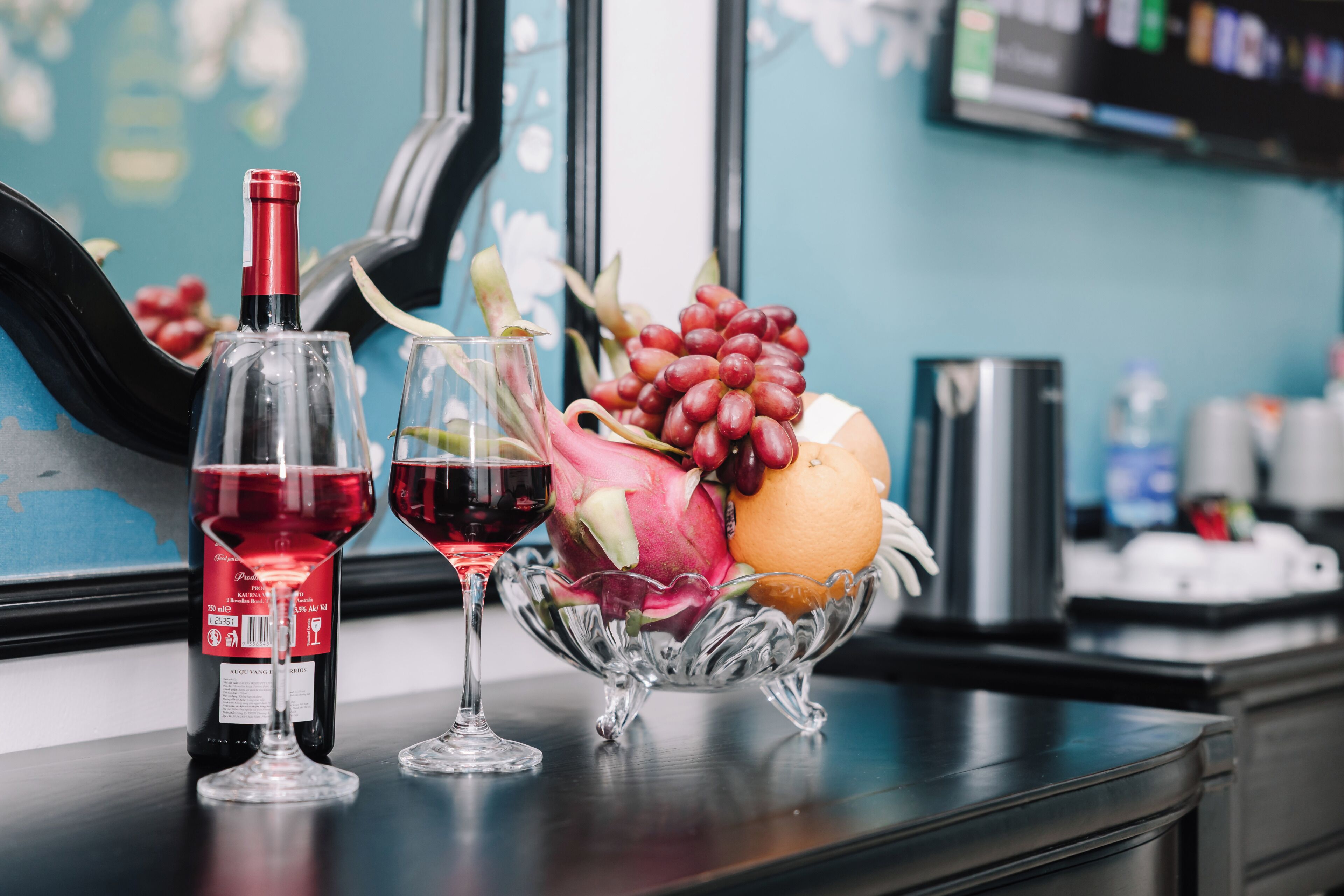 Une bouteille de vin, deux verres et un panier de fruits sur une table.