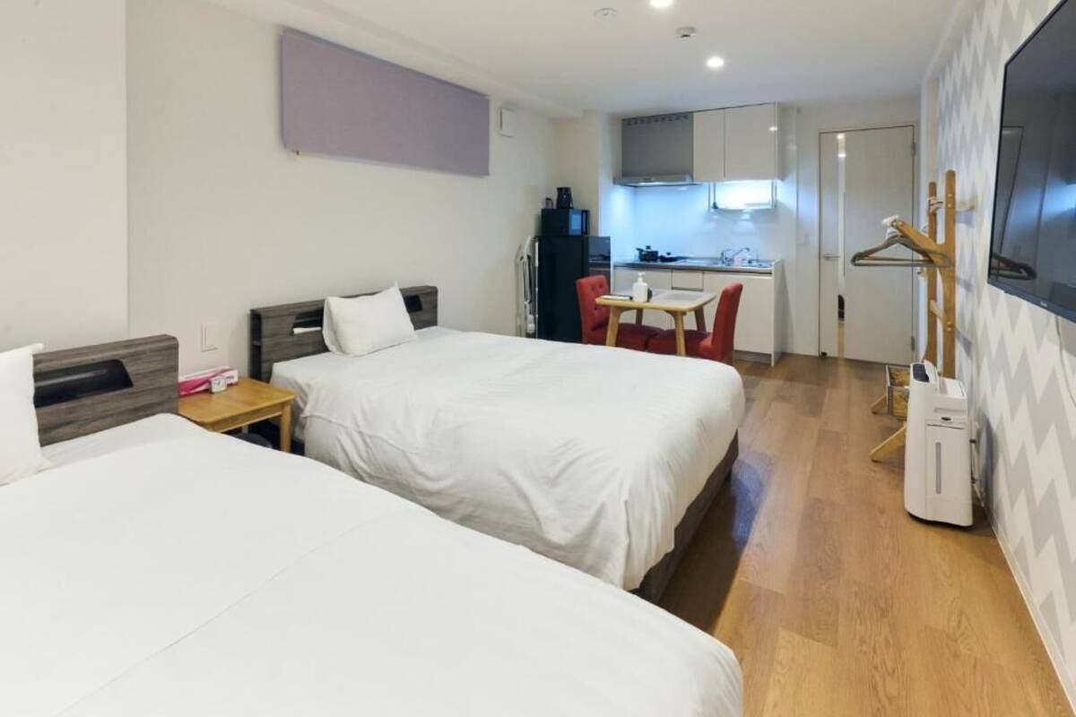 Ein Hotelzimmer mit zwei Betten, einer kleinen Küchenzeile, einem Fernseher und Holzboden.