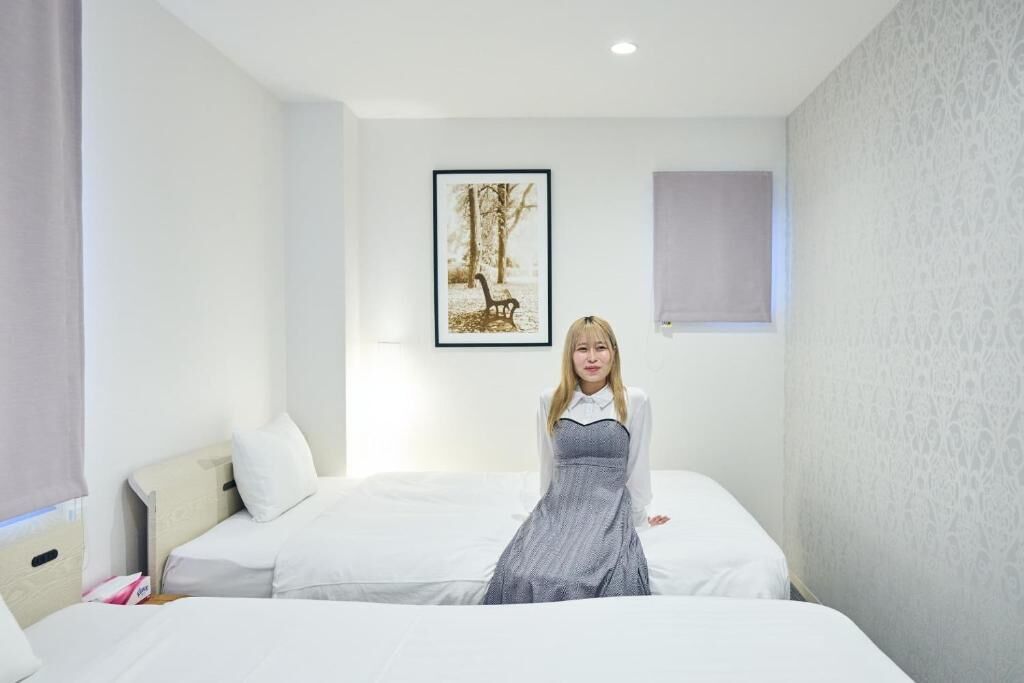 Camera d'albergo con un letto, un comodino, un quadro appeso al muro e una finestra con una tenda.