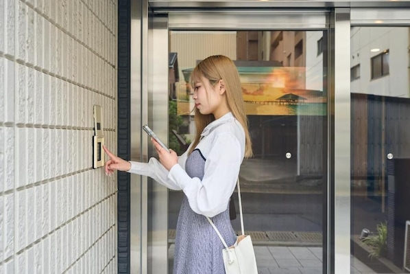 A person standing at a door, holding a phone, and interacting with a doorbell. - Nemuru Kagoshima-Chuo Station (Kagoshima)