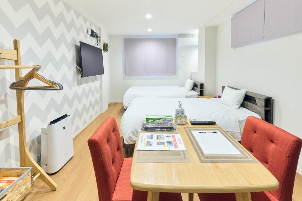 A hotel room with two beds, a TV, a heater, a table with a menu, and a coat rack.