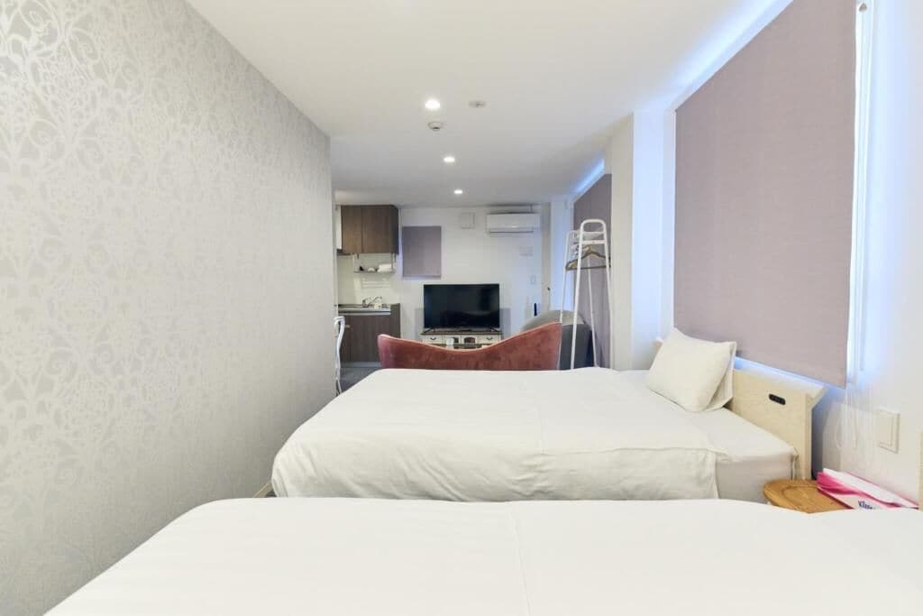 A hotel room with a bed, a TV, a kitchenette, and a window.
