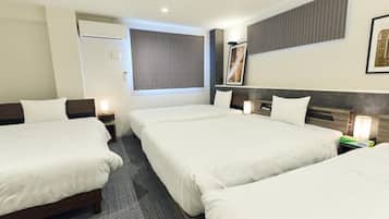 A hotel room with three beds, a large window with blinds, a framed picture on the wall, and a small table with a lamp.