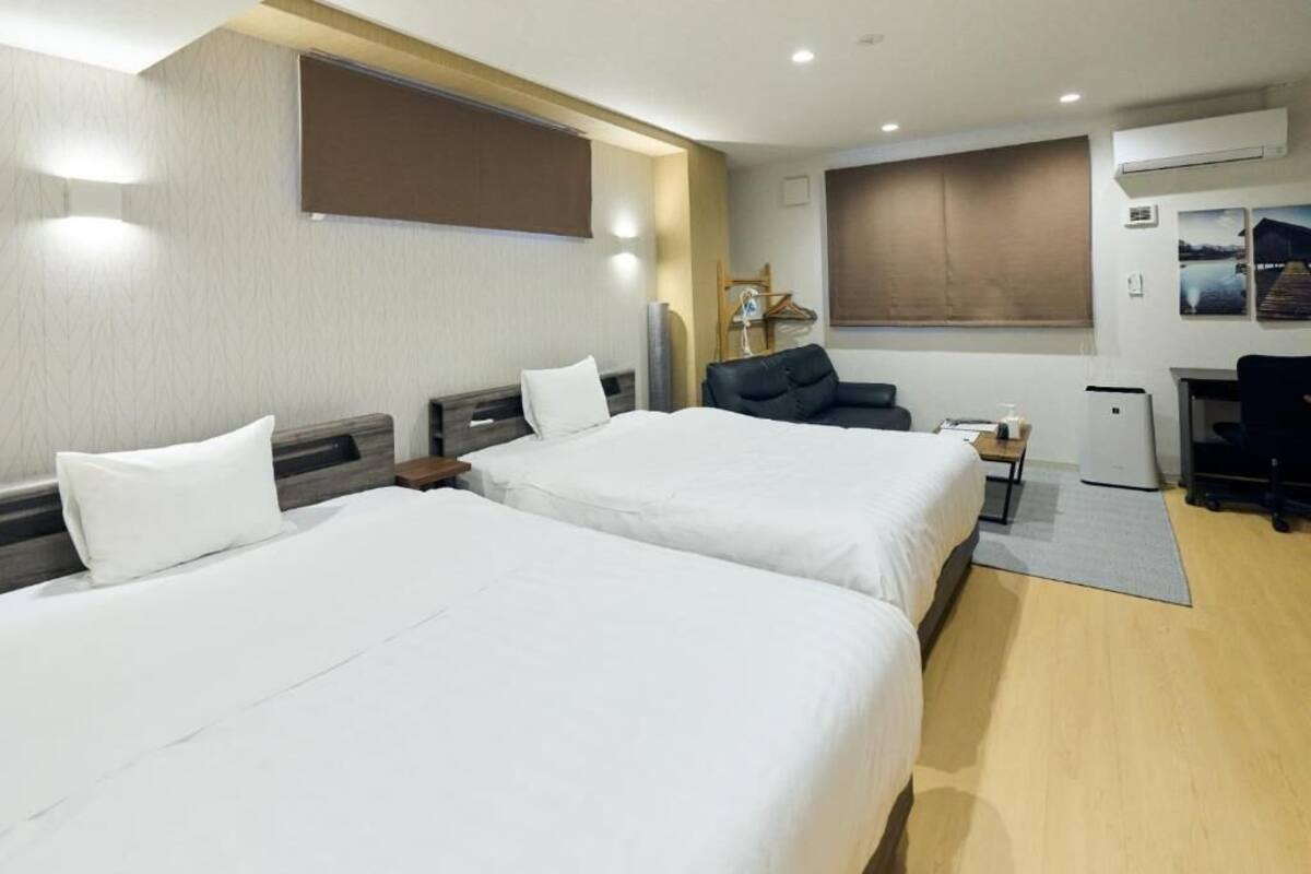 Ein Hotelzimmer mit zwei Betten, einem Schreibtisch, einem Stuhl, einem Fernseher und einem Fenster.