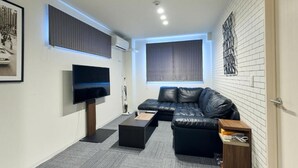 A modern living room with a flat-screen TV, a leather sofa, a coffee table, and a wall-mounted artwork. - Nemuru Kagoshima-Chuo Station (Kagoshima)