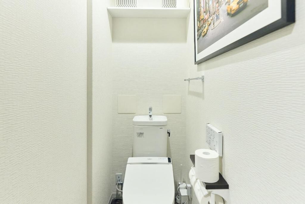 A narrow bathroom with a toilet, sink, and a framed picture on the wall.