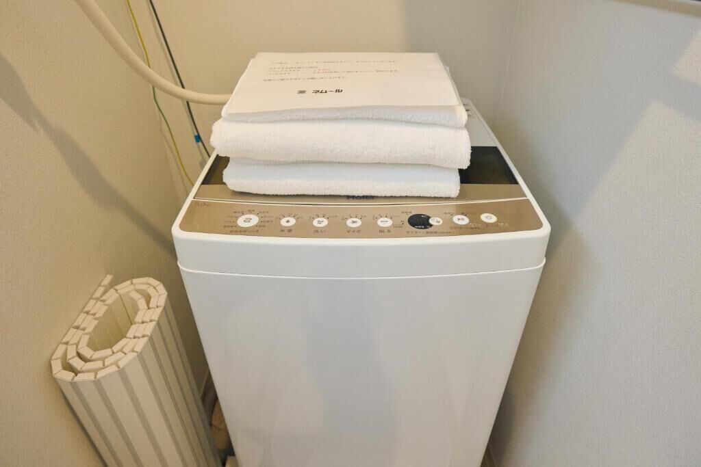 A front-loading washing machine with a control panel, a white towel on top, and a vent on the left.
