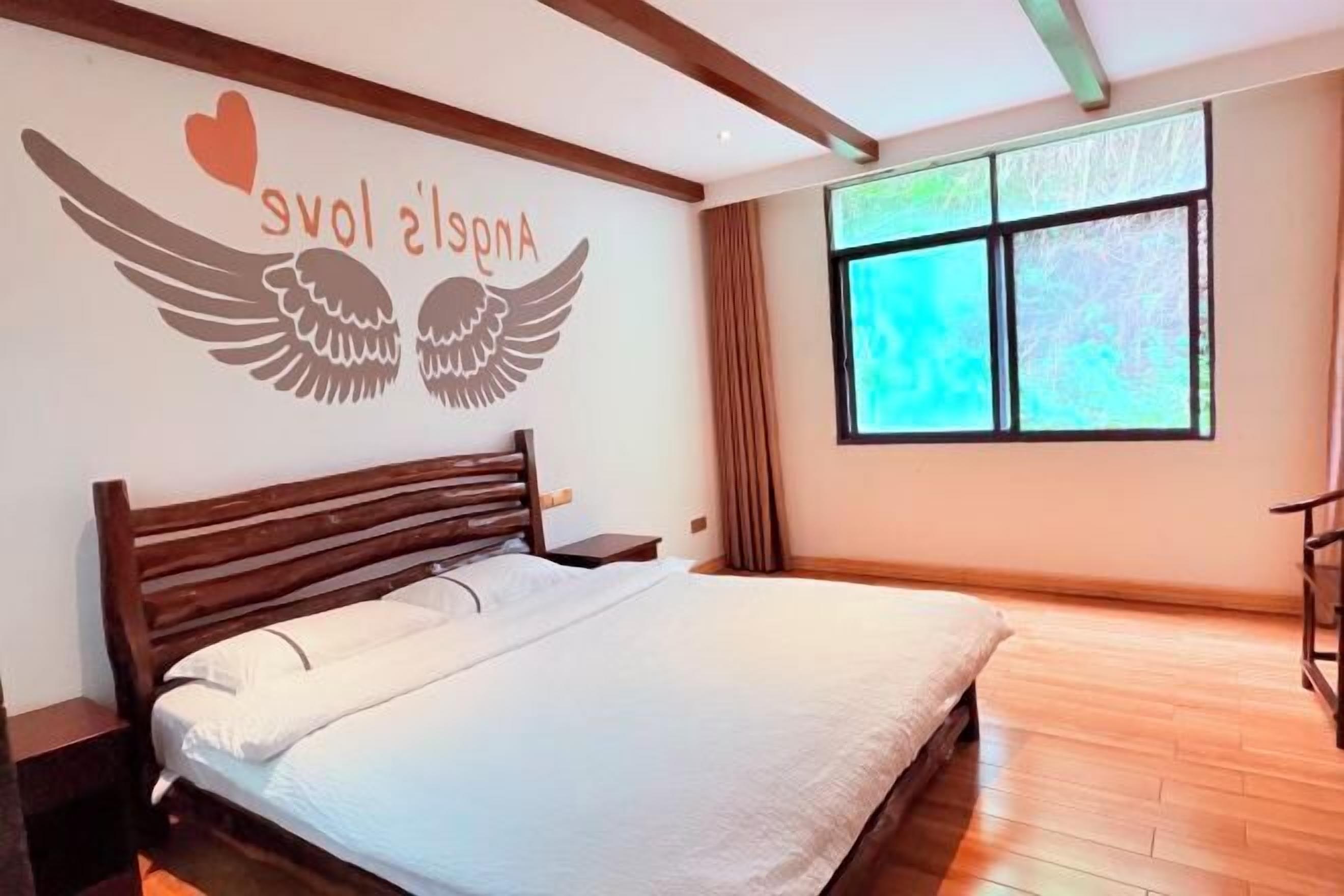 A bedroom with a bed, a nightstand, a window with curtains, and a wall with a winged heart design.