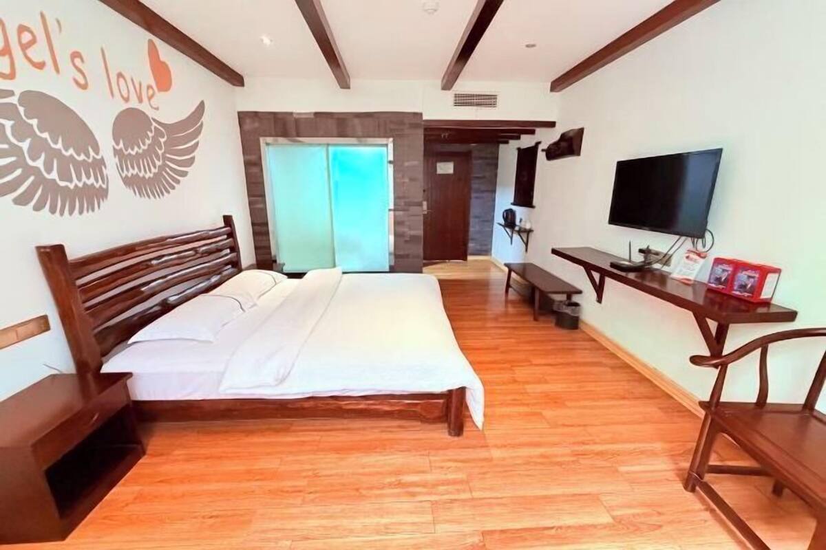 Une chambre à coucher comprenant un lit, une tête de lit en bois, une télévision, un bureau et un mur décoré d’un motif en forme d’aile.