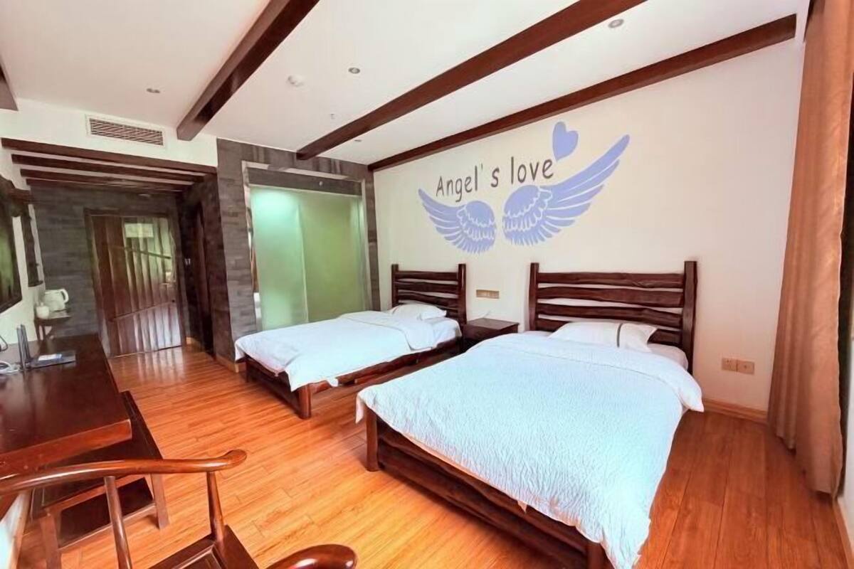 Une chambre d’hôtel avec deux lits, un bureau en bois et un mur orné de l’inscription « L’amour d’Angel » et de cœurs ailés.