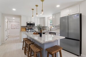 A modern kitchen with white cabinets, stainless steel appliances, a large island with stools, and pendant lighting. - Golden Slumbers, your coastal retreat in Goose Rocks Beach, Kennebunkport (Kennebunkport)