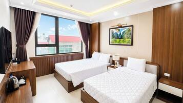 A hotel room with two beds, a desk with a kettle, a TV, and a painting on the wall.