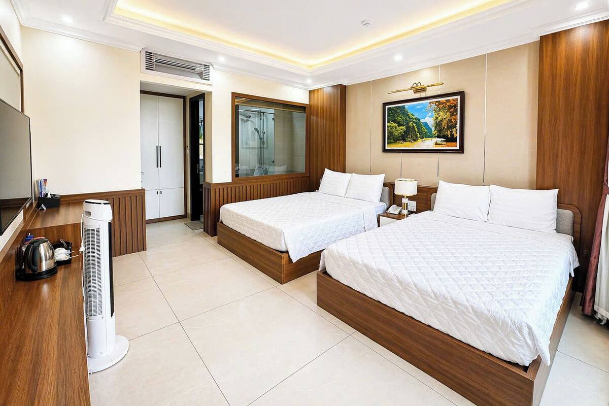 A hotel room with two beds, a TV, a heater, and a bathroom with a shower.