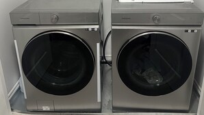 Two Samsung front-loading washing machines in a laundry room with a plain white wall and a tiled floor.