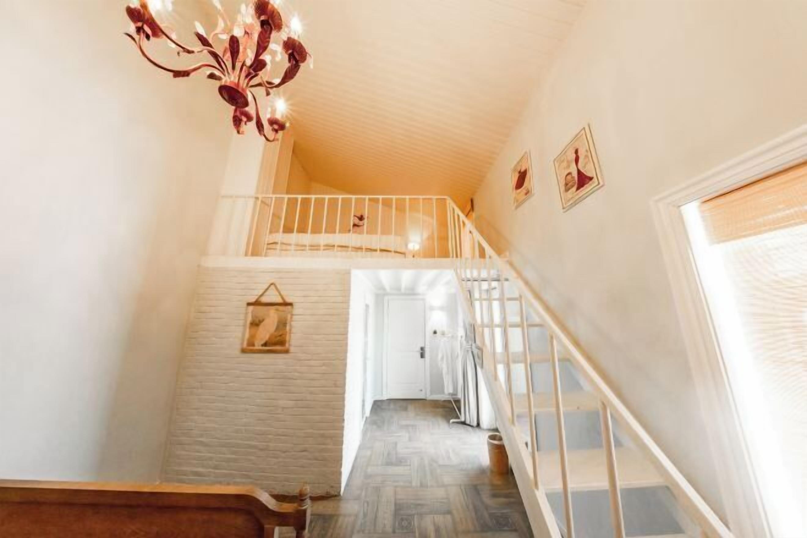 A staircase leading to a second floor with a white railing, a hanging light fixture, and a door at the end.