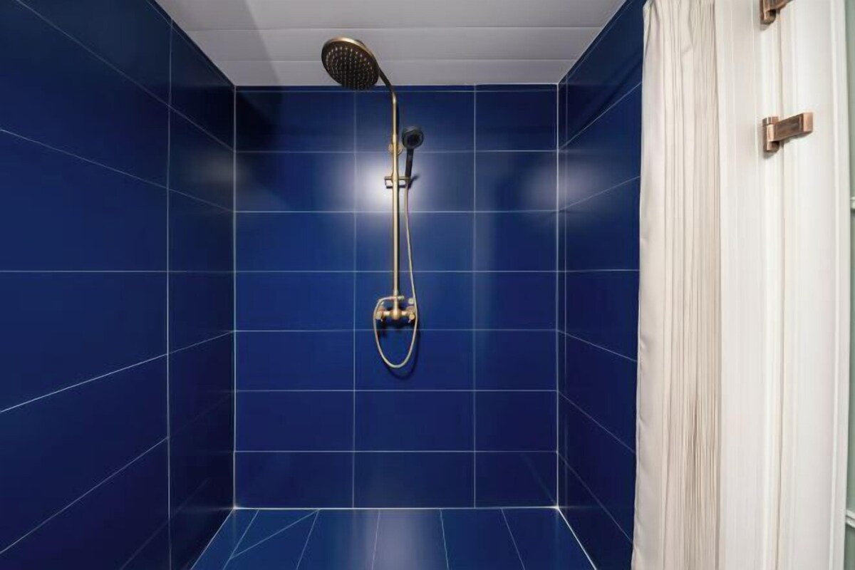 A bathroom with blue tiles, a showerhead, and a white curtain.
