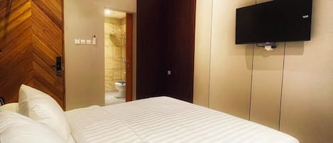 A hotel room with a large bed, a flat-screen TV mounted on the wall, and a wooden door with a chevron pattern.