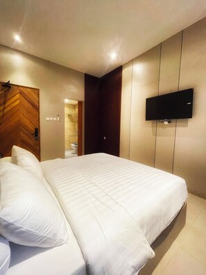 Habitación de hotel con una cama grande, un televisor de pantalla plana montado en la pared y una puerta de madera con diseño en zigzag.