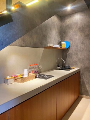 A modern kitchenette with a built-in sink, a coffee machine, and a small shelf with cups and a kettle. - The Foresta By Ohana (Yogyakarta)