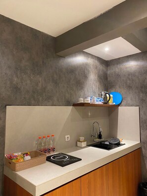 A modern kitchen with a white countertop, a built-in sink, and a wooden cabinet. - The Foresta By Ohana (Yogyakarta)