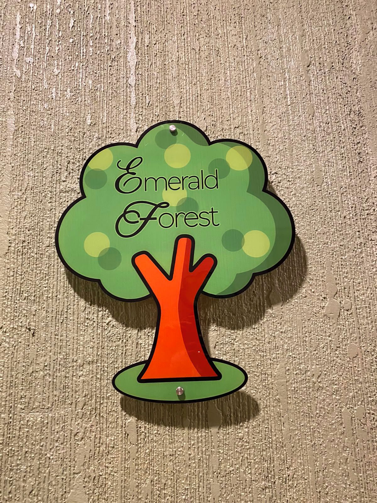 Een bord in de vorm van een boom met de tekst 'Emerald Forest' op een structuurwand.