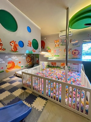 Un área de juegos infantiles con piscina de pelotas, un tobogán y decoraciones en las paredes.