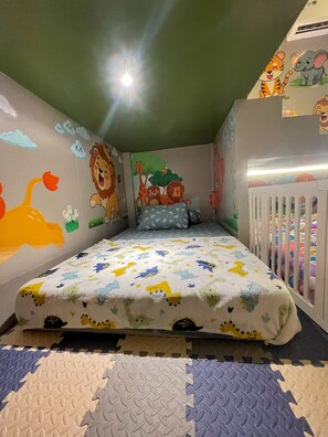 A child's bedroom with a bed, colorful wall murals, a crib, and a playpen. - The Foresta By Ohana (Yogyakarta)