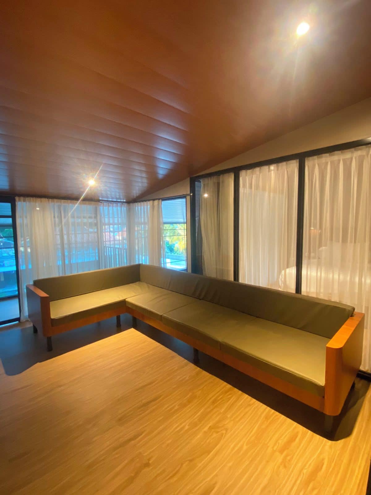 Una sala de estar moderna con un banco de madera, ventanas amplias con cortinas traslúcidas y un techo inclinado.