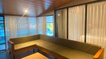 Una sala de estar moderna con un banco de madera, ventanas amplias con cortinas traslúcidas y un techo inclinado.