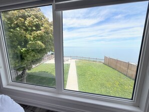 A window with a view of a grassy yard, a wooden fence, and a body of water. - Lakeview retreat closer to Toronto and Niagara Area (Hamilton)