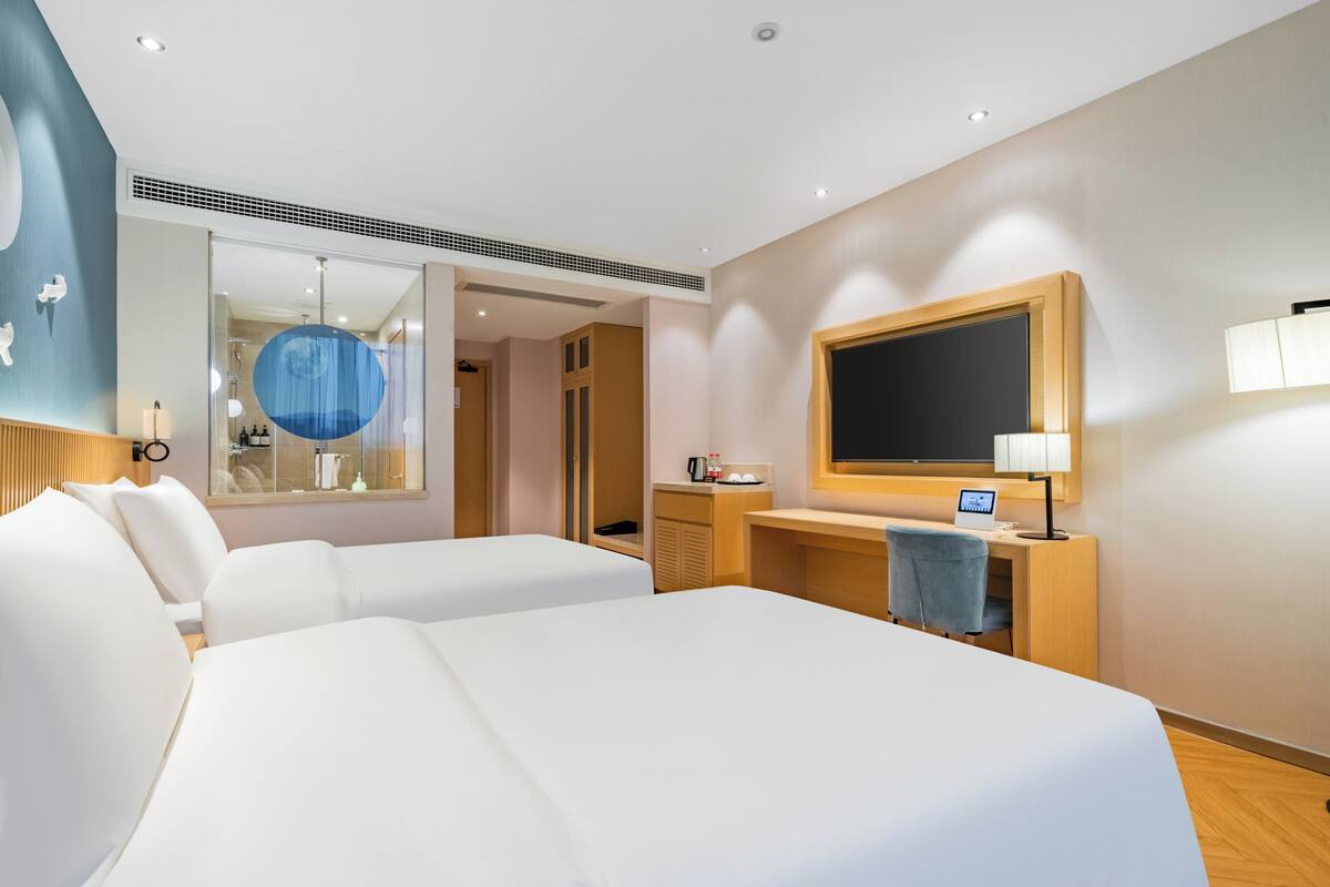 A hotel room with two beds, a desk with a computer, a mirror, and a window.