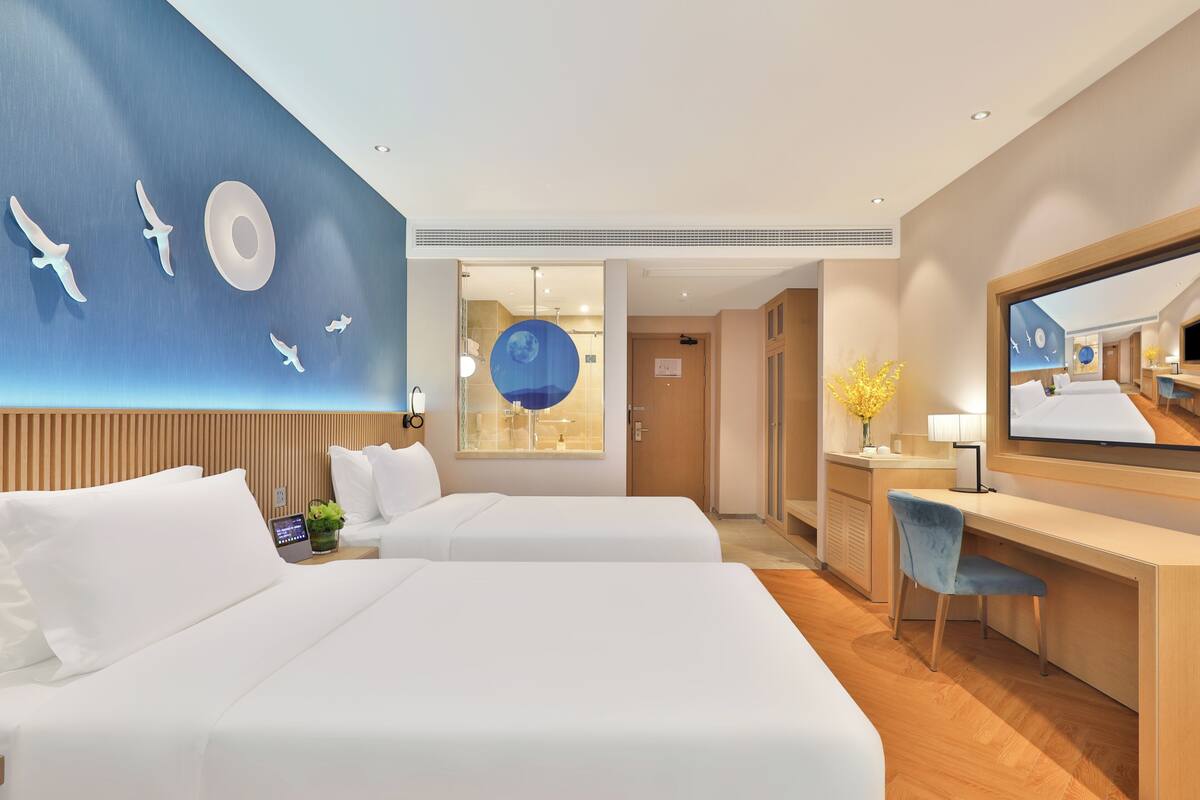 A hotel room with two beds, a desk, a TV, and a wall with a circular design.