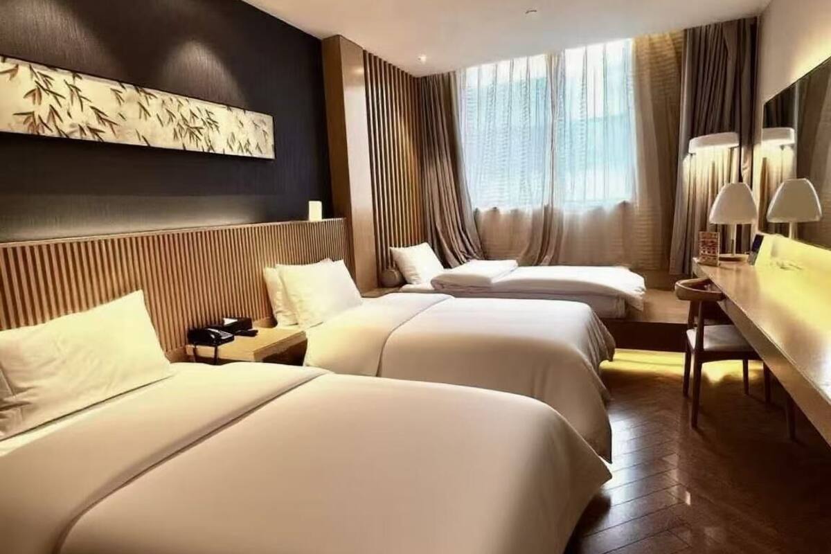 A hotel room with two beds, a desk, a chair, a lamp, and a large window with curtains.