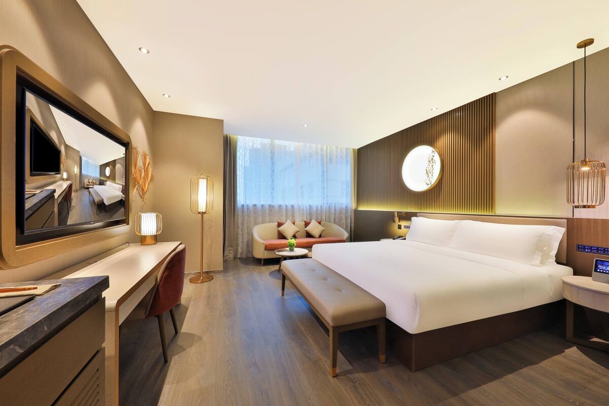 A modern hotel room with a large bed, a desk, a sofa, and a TV.