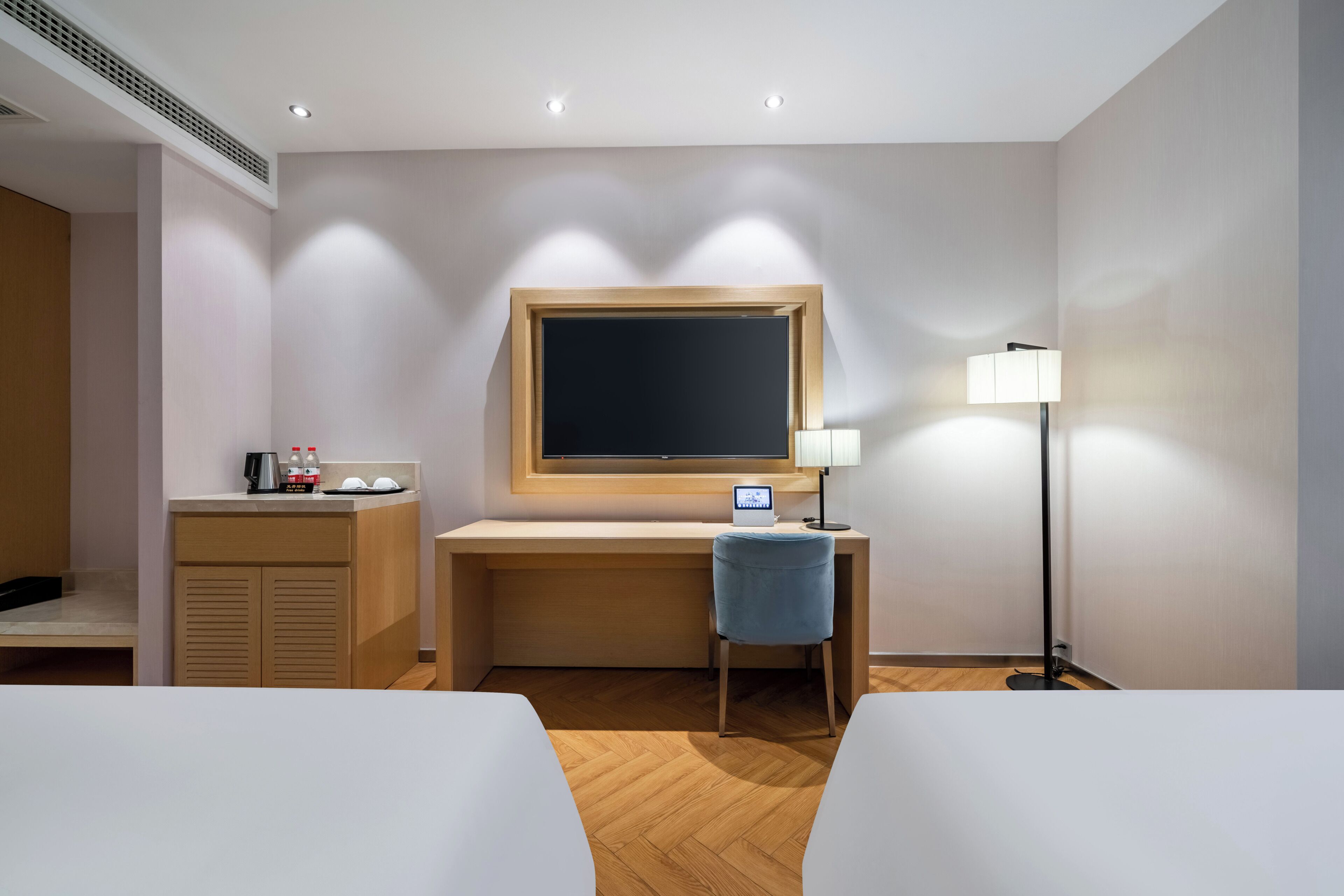 A hotel room with a desk, chair, lamp, and two beds.