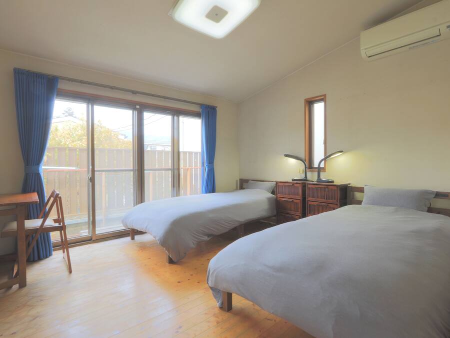 A room with two beds, a desk, and a chair. There is a sliding glass door leading to an outdoor area.