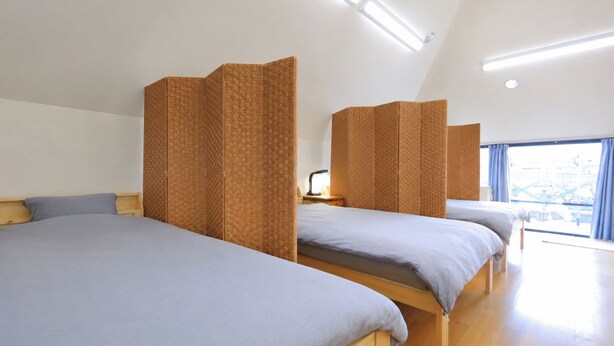 A modern hotel room with a sloped ceiling, wooden flooring, and a large window providing a view of the city. - Hostel Five (Kochi)