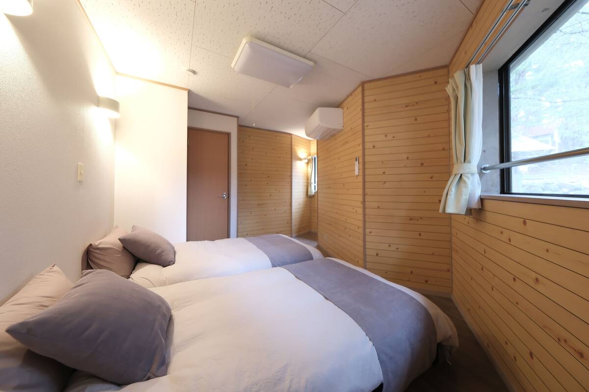 A room with two beds, wooden walls, a window, and a ceiling light.